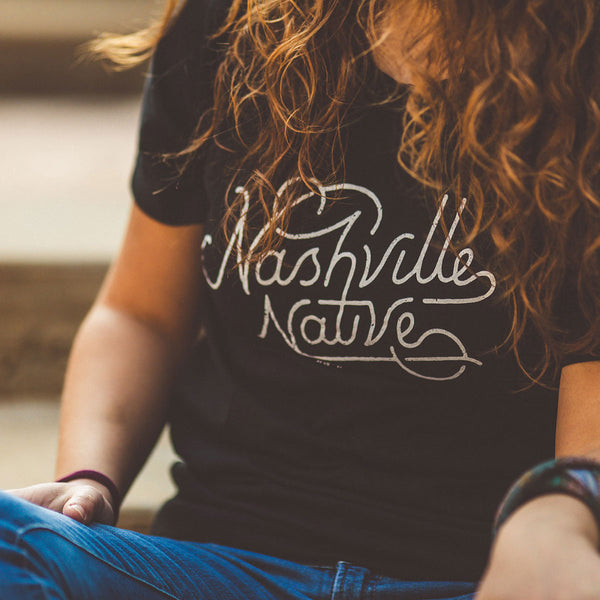 Model sitting wearing the Nashville Native T-shirt in Heather black