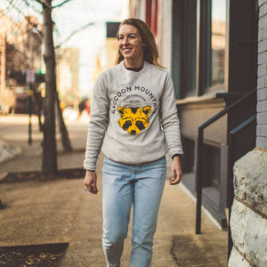 Model walking in downtown Chattanooga wearing our Bella Canvas heather dust crewneck featuring our NativeMade Raccoon Mountain Chattanooga design.