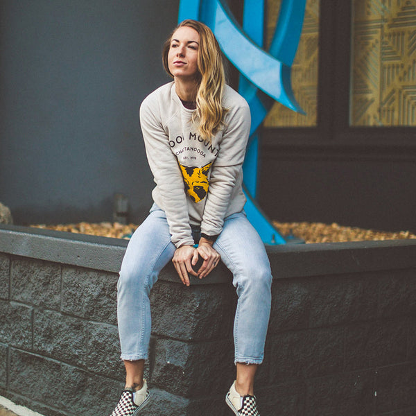 Model sitting in downtown Chattanooga wearing our Bella Canvas heather dust crewneck featuring our NativeMade Raccoon Mountain Chattanooga design.